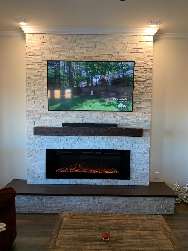 White stacked-stone fireplace wall with electric insert, dark mantel and TV